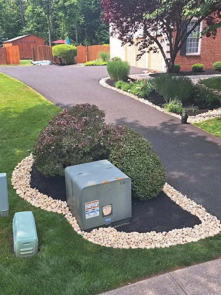 White river stone border around a mulched shrub bed beside a curved asphalt driveway