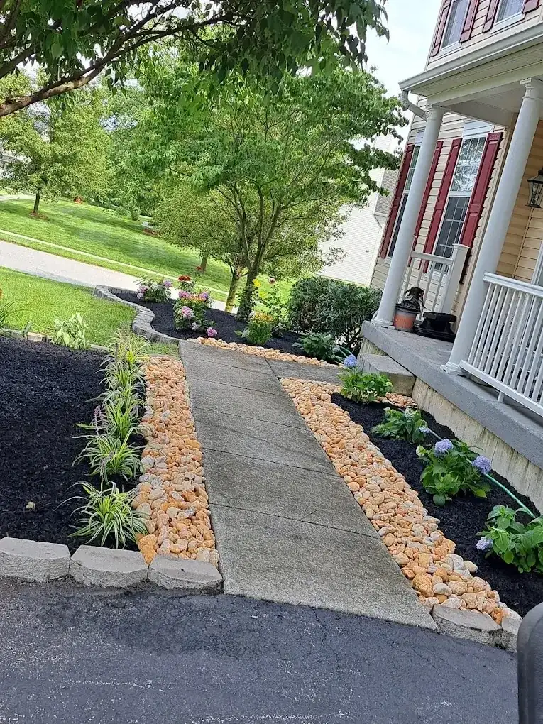 Front walkway lined with tan river stone borders and black mulch flower beds beside a porch